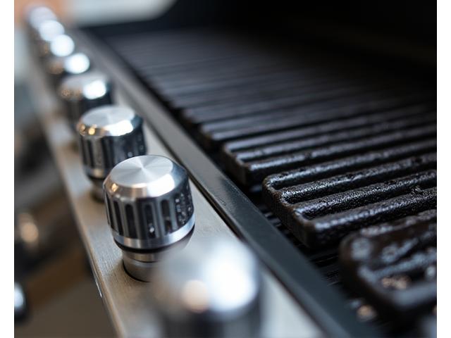 Close-up of a high-end gas grill with stainless steel features, showing precise temperature dials and a large grilling surface.